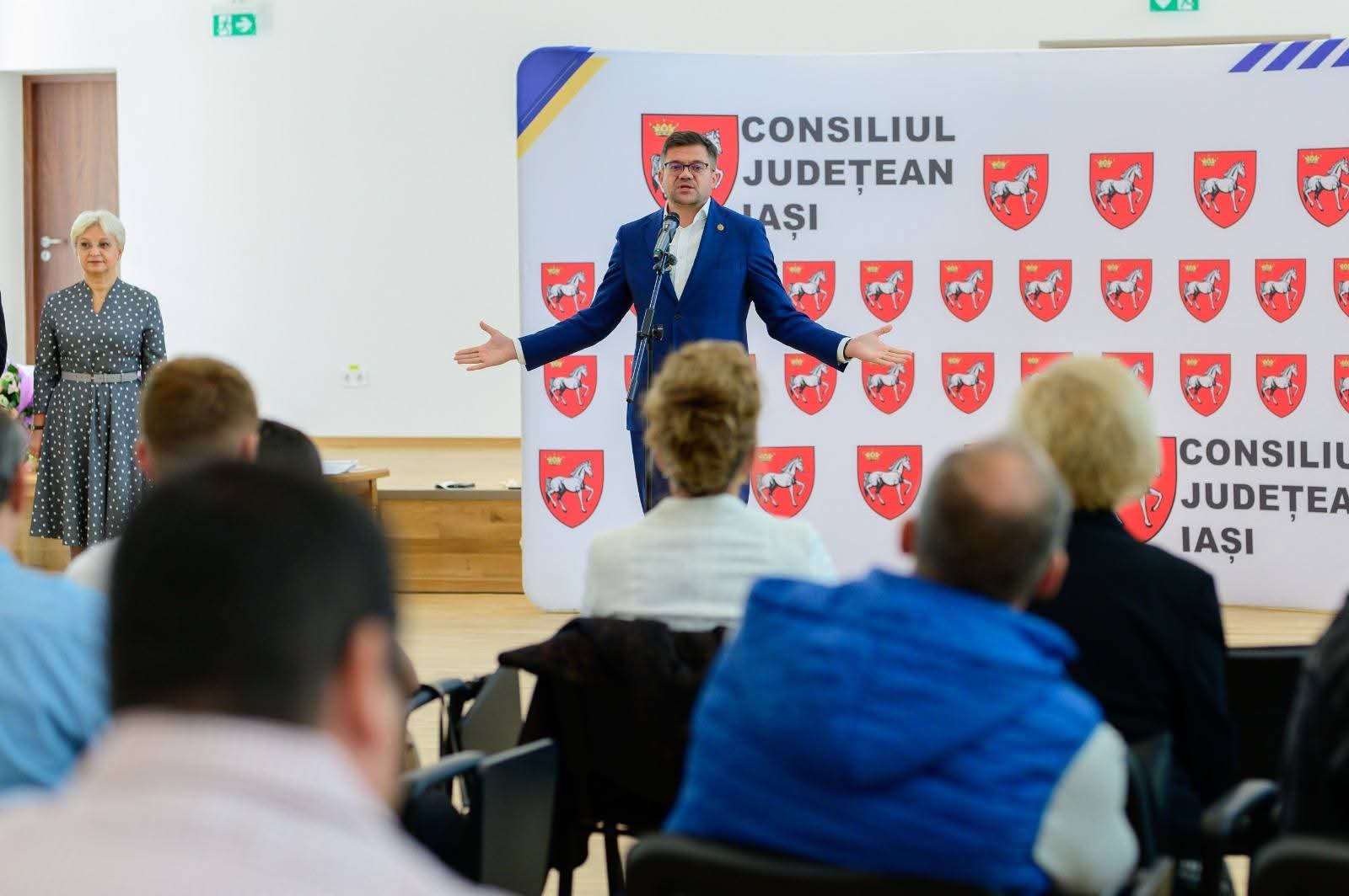 Vorbitor pe scena ceremoniei, în fața unui panou cu sigla Consiliului Județean Iași