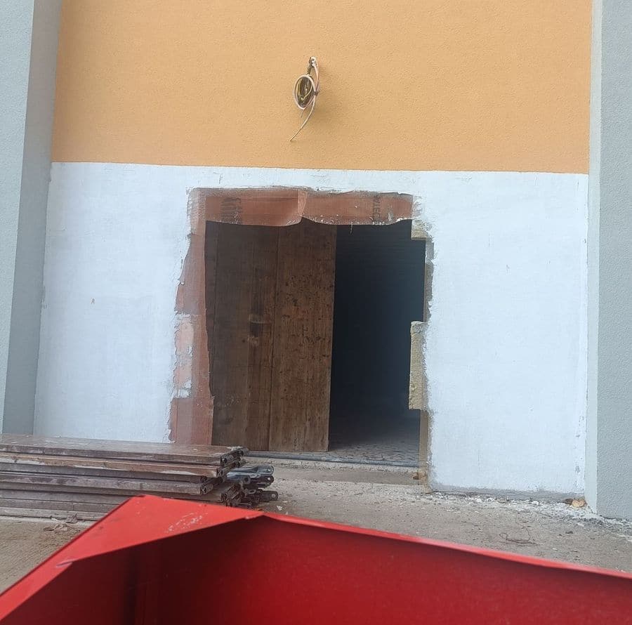 Fațada vopsită a clădirii Cinema Dacia, cu o deschidere tăiată în perete, panouri de lemn în interior și materiale depozitate în față