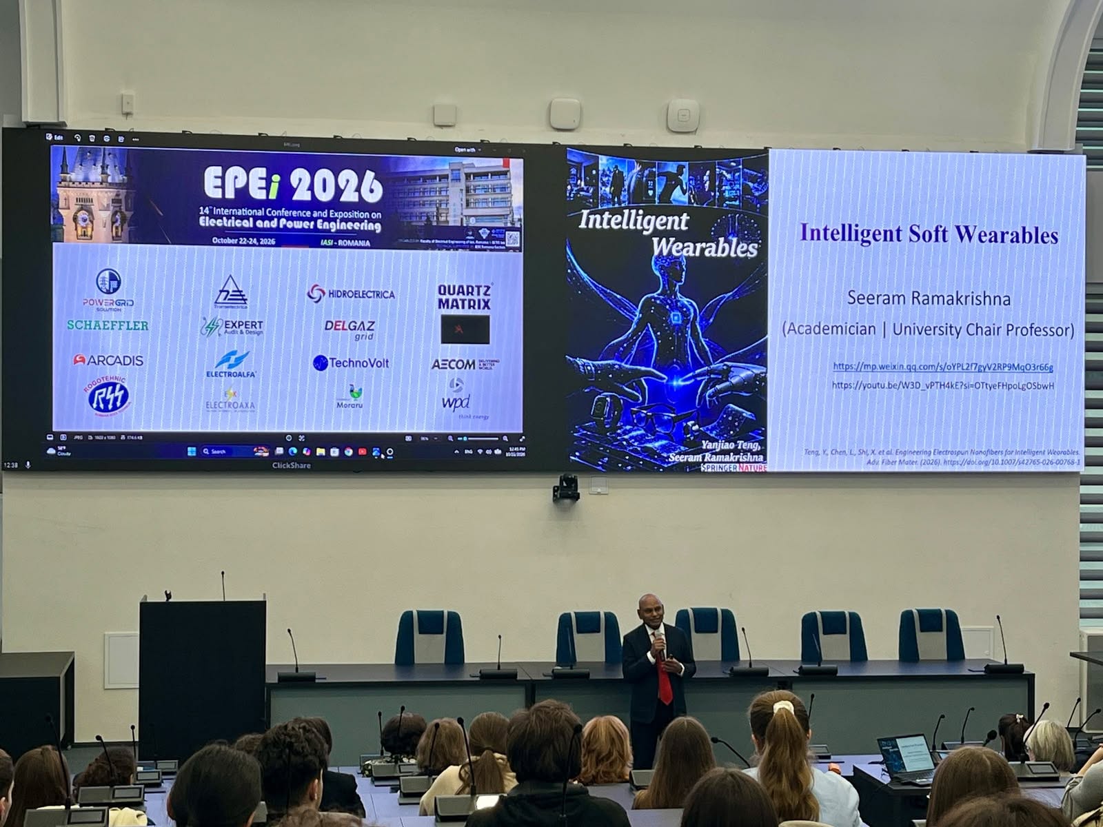 Bărbat în costum, cu microfon în mână, în fața unor ecrane mari pe care sunt proiectate sigla conferinței EPEi 2026 și un slide intitulat Intelligent Soft Wearables