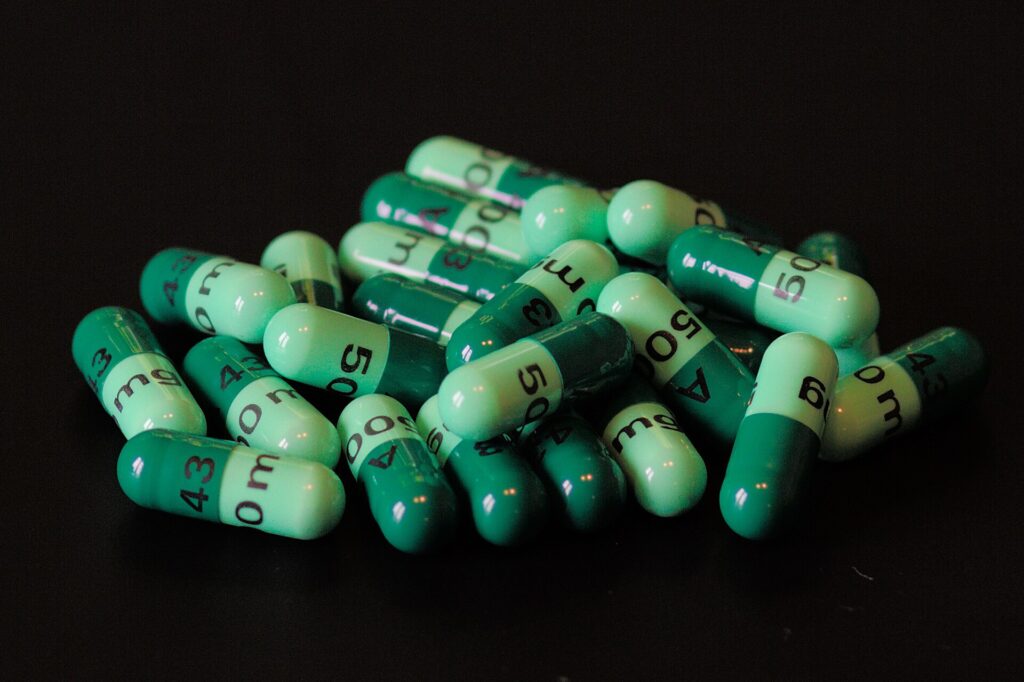 Capsule verzi de antibiotic, cefalexină, așezate grămadă pe un fundal negru