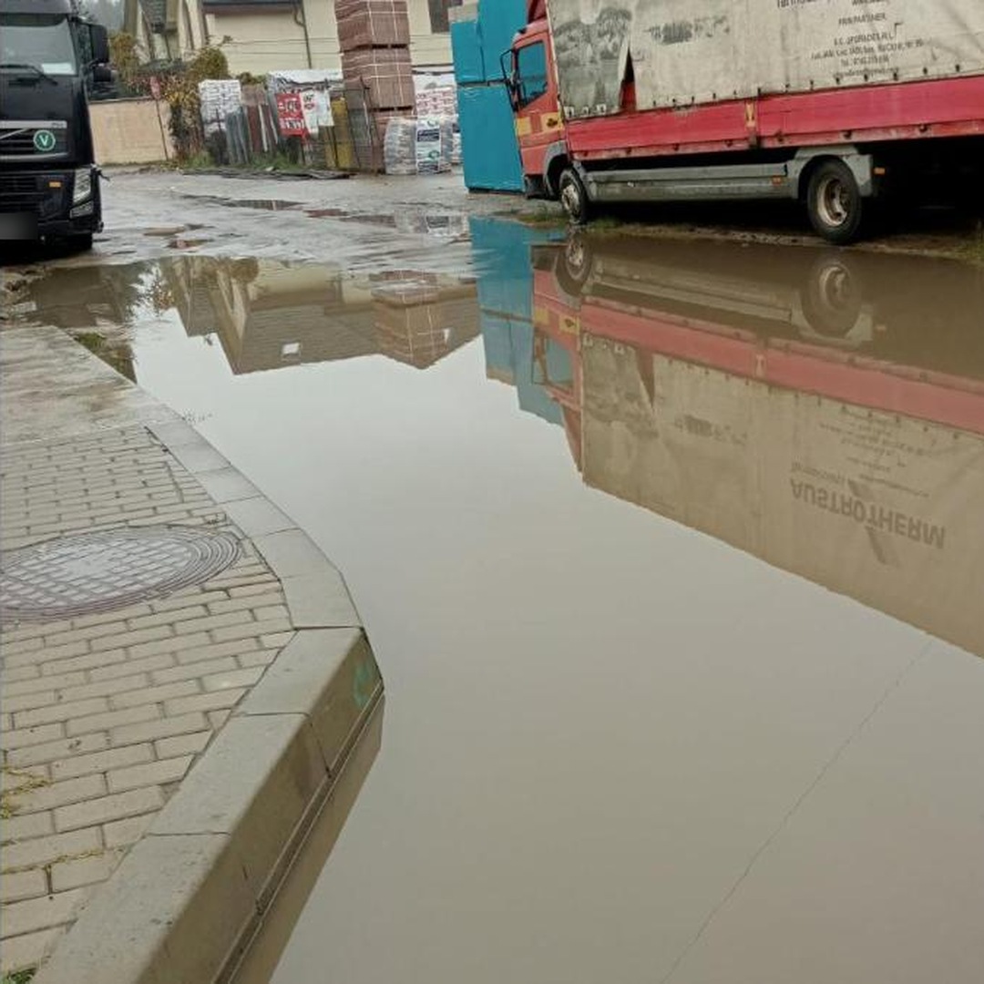 Băltoacă lângă un trotuar din Bucium, cu un camion parcat și materiale de construcții în fundal