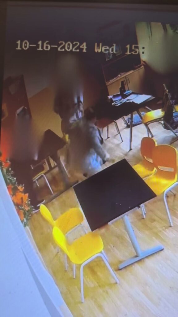 Captură din filmare: o persoană cade între mese, într-o sală de clasă, chipurile sunt estompate