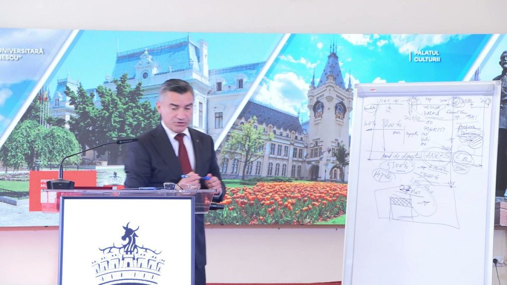 Mihai Chirica lângă un flipchart cu o schemă desenată, la o conferință de presă