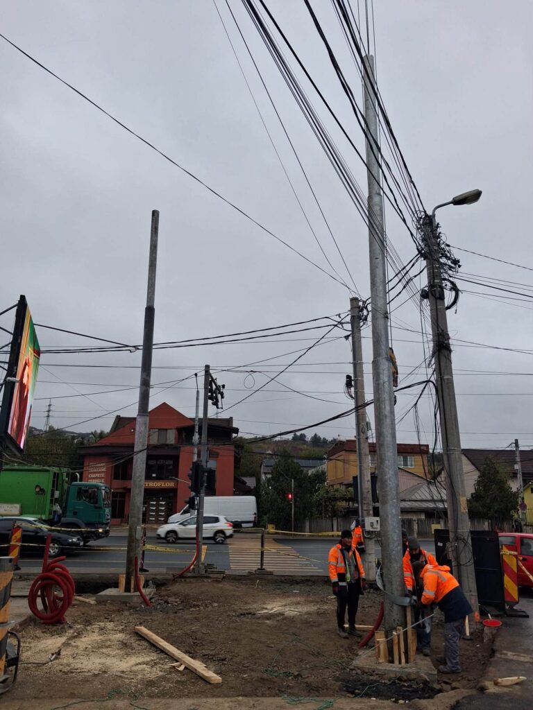 Muncitori montează un stâlp metalic nou lângă stâlpii vechi de beton, la intersecția Bucium–Trei Fântâni