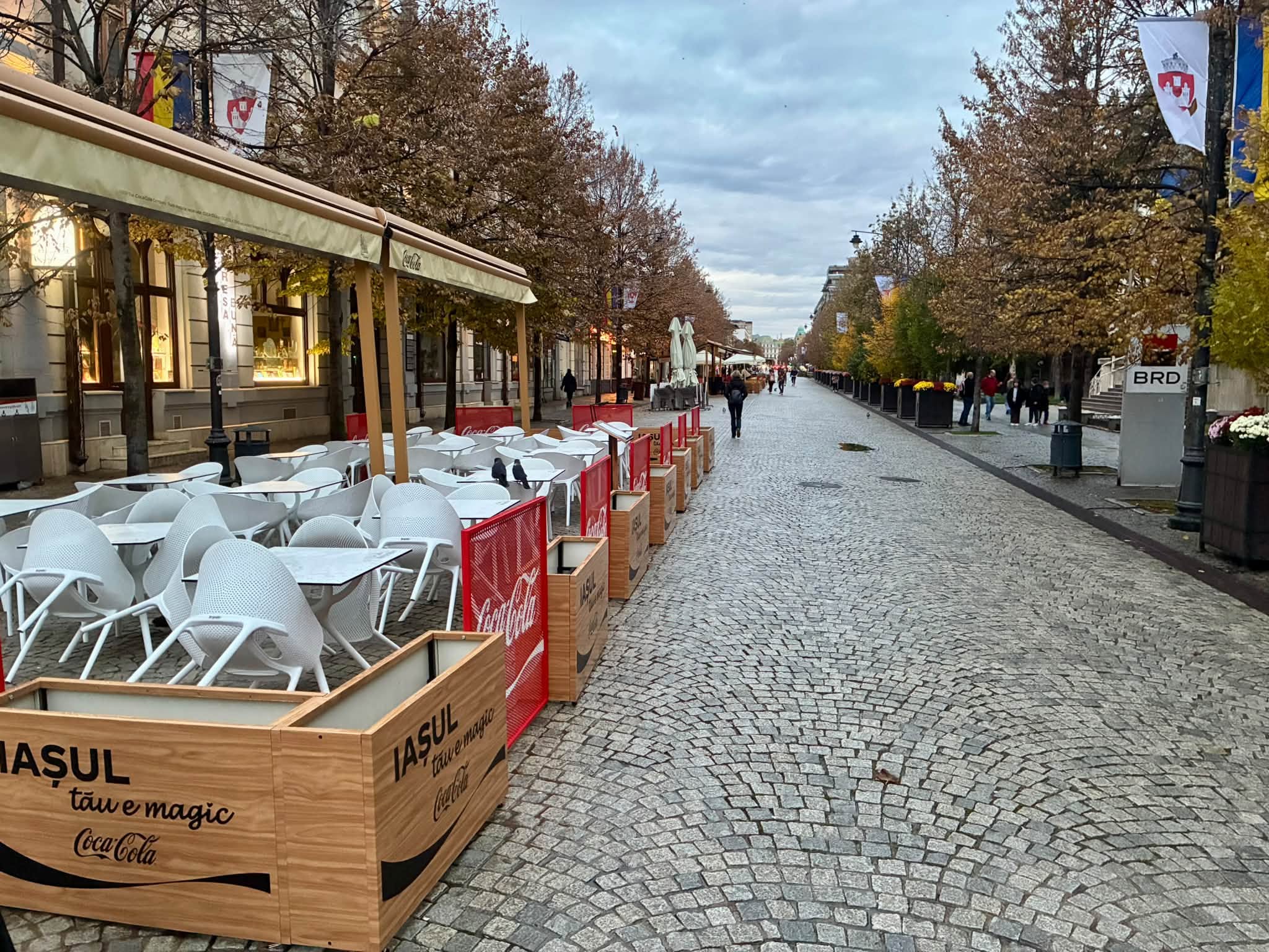 Împrejmuiri de lemn și panouri roșii cu reclame în jurul unei terase de pe pietonalul Ștefan cel Mare